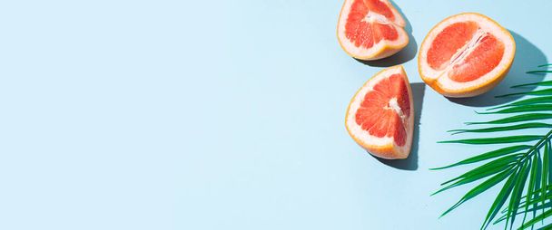 cut halves of a grapefruit and a leaf of a palm tree on a blue background. Top view, flat lay. Banner. - Фото, зображення