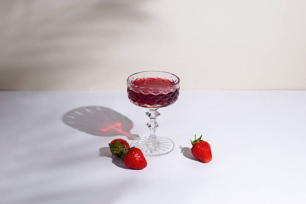 vidro com vinho tinto e morangos na mesa em um fundo claro. - Foto, Imagem