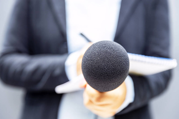 Journalist holding microphone at news conference or media event and writing notes - Foto, imagen