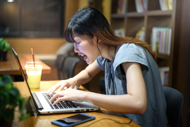  Συναισθηματικό άγχος Όμορφη Ασιάτισσα φοιτήτρια γυναίκα φωνάζει και εργάζεται σε φορητό υπολογιστή στη σύγχρονη αίθουσα βιβλιοθηκών  - Φωτογραφία, εικόνα