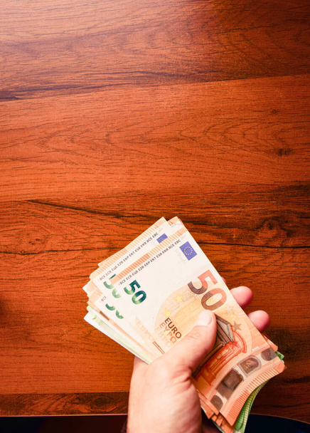 Kädessä on 50 euron setelipino puupöydän taustaa. Palkat ja vähimmäispalkka Euroopan unionissa. - Valokuva, kuva