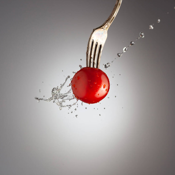 ripe cherry tomato on a fork poured water, water splashes, black white background, gradient - Foto, immagini