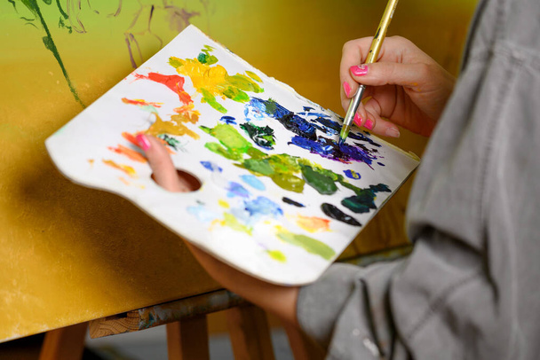 Γυναίκα Καλλιτέχνης αναμιγνύει χρώματα στην παλέτα, ζωγράφος στο στούντιο, δημιουργός κάνει το έργο τέχνης. - Φωτογραφία, εικόνα