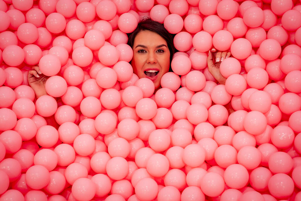 Una hermosa modelo asiática juega en una habitación colorida con una gran cantidad de bolas de plástico - Foto, Imagen