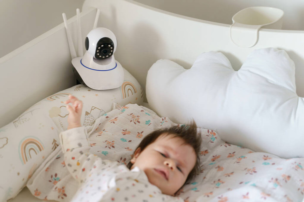 Bewakingscamera op babybed thuis in de slaapkamer kijken naar klein kind in wieg tijdens het slapen - Foto, afbeelding