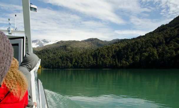 catamaran rijden door de groene wateren in de buurt van puerto blest, mensen kijken naar het meer en de bergen op vakantie in de buurt van bariloche - Foto, afbeelding