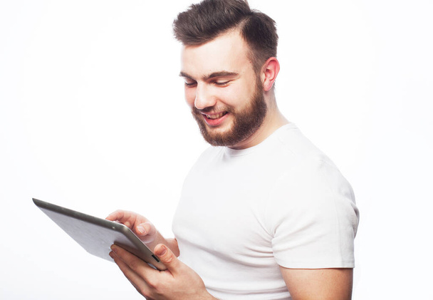 Tehnology, people and lifestyle concept: young bearded man wearing white t-shirt using a tablet computer - isolated over a white background - Foto, Imagem