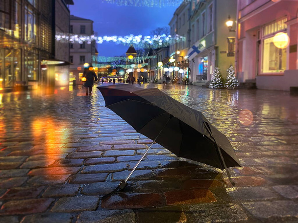 rainy evening  street  Christmas black umbrella on wet pavement city medieval  light blurred decoration people wakl holiday in Tallinn old town Estonia  - Photo, Image