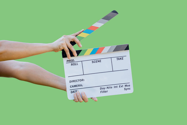 Χέρι κρατώντας ταινία πίνακα χρωμάτων σχιστόλιθο για τον κινηματογράφο και την τηλεοπτική βιομηχανία σε πράσινο φόντο - Φωτογραφία, εικόνα