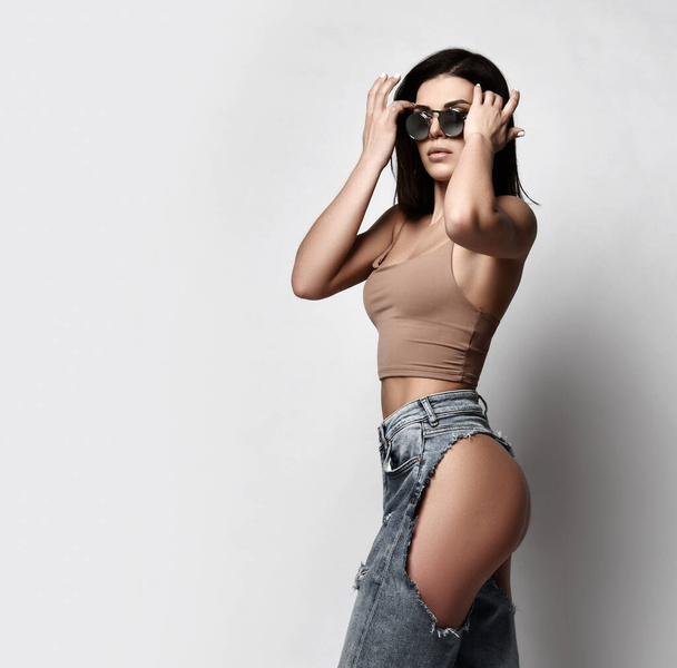 Self-confident sexy adult woman is walking in torn jeans with naked butt, ass, sunglasses and top. Side view - Fotoğraf, Görsel