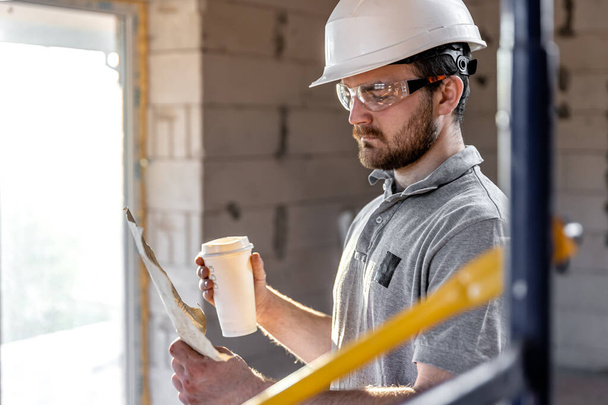 Ein Elektriker studiert mit einem Kaffee in der Hand eine Bauzeichnung. - Foto, Bild