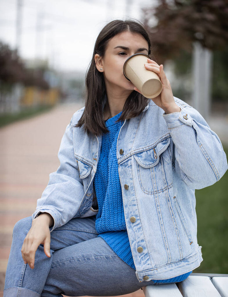 Young woman drinking coffee to go sitting on a bench in the park .. - Photo, Image