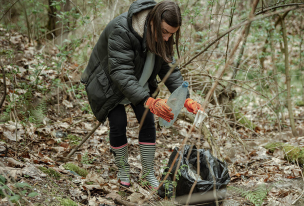 A volunteer girl with a garbage bag cleans up garbage in the forest. - Zdjęcie, obraz
