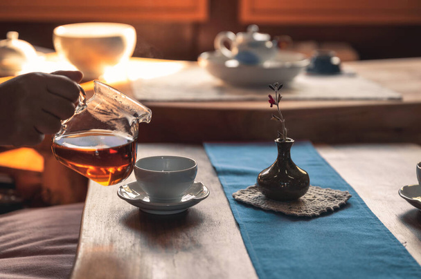 Рука женщина наливает горячий чай в чашку с цветочной глиняной вазой по утрам - Фото, изображение