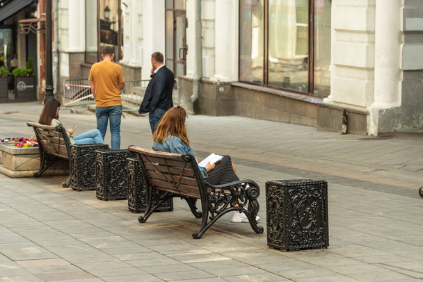 Moskau, Russland, 27. Juli 2020 - Normales Stadtleben, junge Frauen sitzen auf Bänken und schauen in ein Notizbuch mit Notizen und einem Smartphone in einer Fußgängerzone der Stadt - Foto, Bild