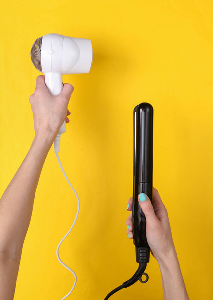 Hands holding White hair dryer and hair straightener on yellow background. Beauty concept. Top view. Flat lay - Photo, Image
