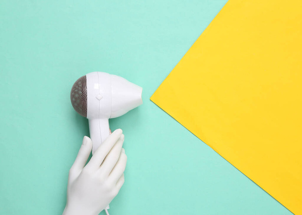 Hand holding hair dryer on yellow blue paper background. Minimalism fashion layout. Top view. Copy space - Foto, immagini