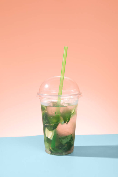 homemade non-alcoholic mojito on a blue table and pink background. summer refreshing drink with ice and a straw. - Foto, imagen