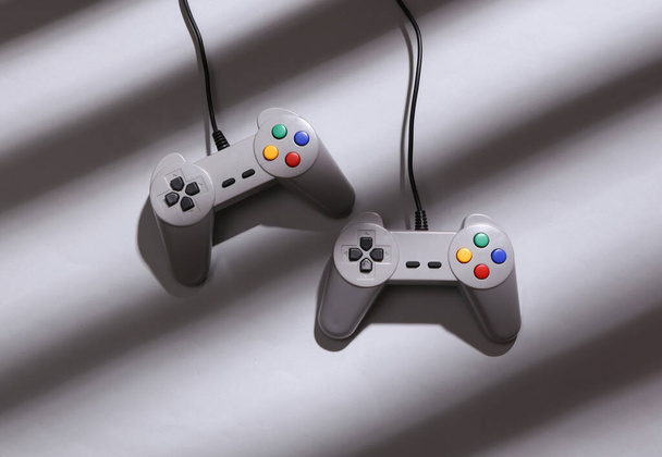 Minimalistic layout. Retro gamepads with long striped trendy shadows on gray background. Top view - Photo, Image