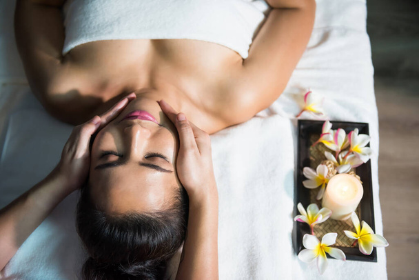 Visão de retrato superior de óleo tailandês Massagem facial ayurvédica na cama para mulher bonita asiática. Tratamento facial anti-envelhecimento por massageador profissional. Menina com terapia de medicina alternativa. - Foto, Imagem