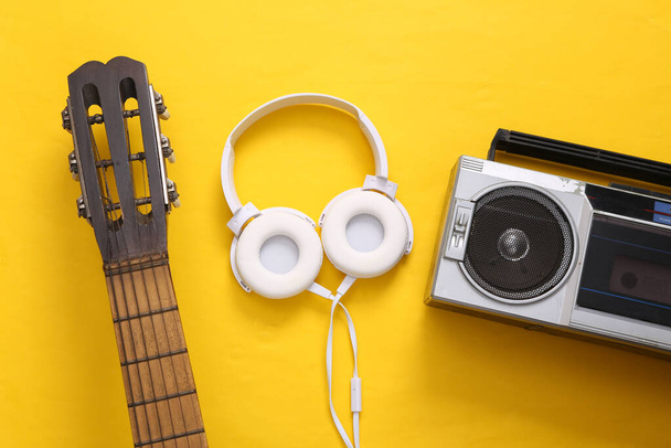 Platte muziek stilleven. Akoestische gitaar hals, audio cassette speler en koptelefoon op gele achtergrond. Muzikaal concept. Bovenaanzicht. - Foto, afbeelding
