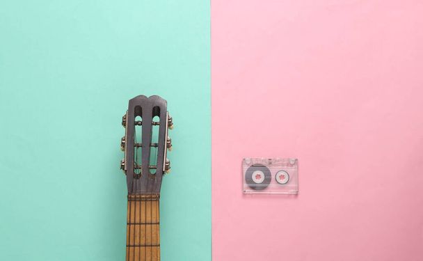 Cuello de guitarra acústica y casete de audio sobre fondo azul rosado. Concepto musical. Minimalismo. Vista superior. Puesta plana - Foto, Imagen