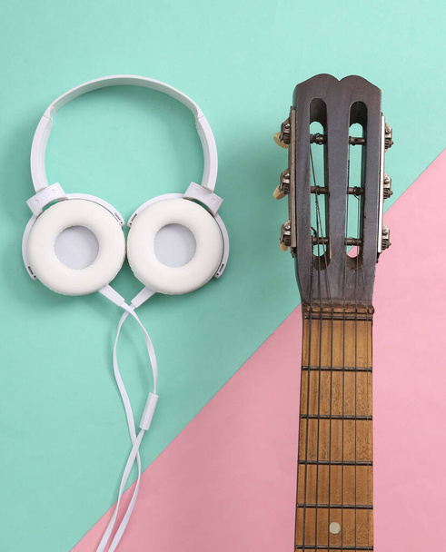 Akustický kytarový krk a sluchátka na růžovém modrém pozadí. Online lekce kytary. Hudební koncept. Horní pohled. Plocha - Fotografie, Obrázek
