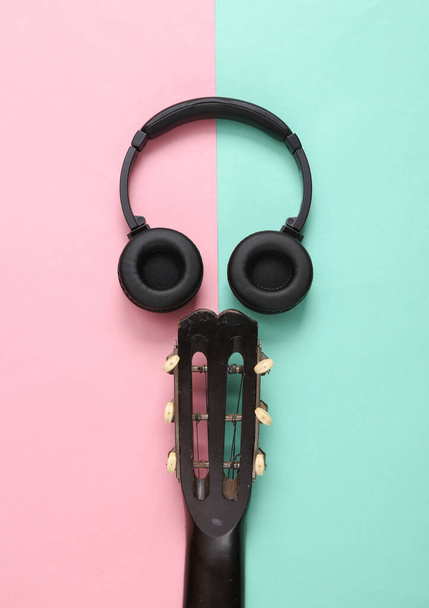 Cuello de guitarra acústica y auriculares sobre fondo azul rosado. Clases de guitarra online. Concepto musical. Vista superior. Puesta plana - Foto, Imagen