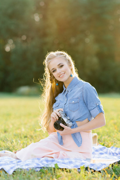 A beautiful young woman holds a retro camera in her hands. Summer picnic - Φωτογραφία, εικόνα