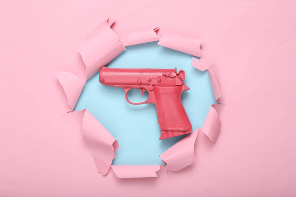 Pinke Pistole vor blau-rosa zerrissenem Hintergrund. Kreatives Konzept. Minimalismus lag flach. Minimales Layout.Draufsicht - Foto, Bild