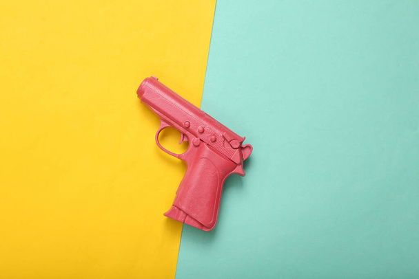 Pink pistol gun on blue yellow background. Creative concept. Minimalism Flat lay. Minimal layout.Top view. Copy space - Photo, Image