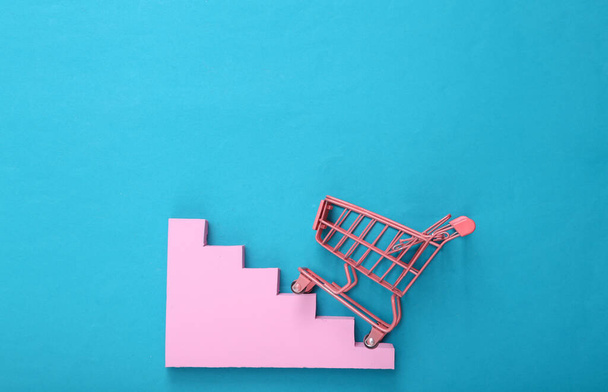 Mini pink supermarket trolley with stairs on blue background. Top view. Minimalism. Flat lay - Photo, Image