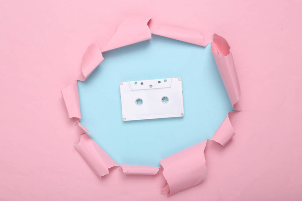 Kreatives Musiklayout. Weiße Audiokassette durch zerrissenes Loch aus rosa blauem Papier. Pastellfarbentrend. Frische Idee. Minimalismus. Konzeptkunst. Flach lag er. Ansicht von oben. - Foto, Bild