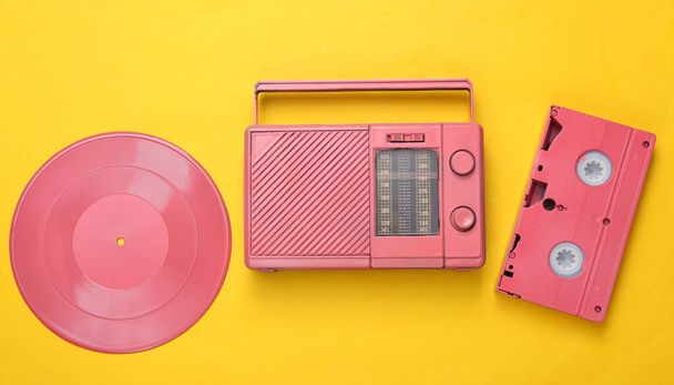 Różowy chłodny odbiornik radiowy, kaseta wideo i płyta winylowa na żółtym tle. Minimalna koncepcja muzyczna. Widok góry. Układy płaskie - Zdjęcie, obraz