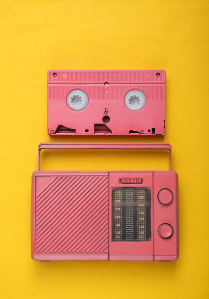 黄色の背景にピンクのラジオ受信機とビデオカセット。最小限のレトロなコンセプト。最上階だ。平敷 - 写真・画像