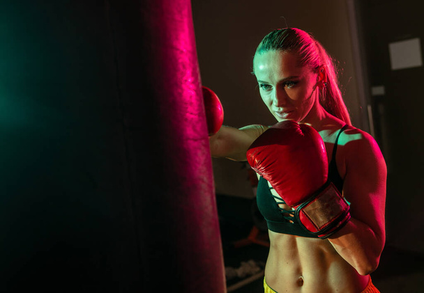 Přizpůsobit žena box boxovací pytel s boxerskými rukavicemi v růžové zelené neonové světlo - Fotografie, Obrázek