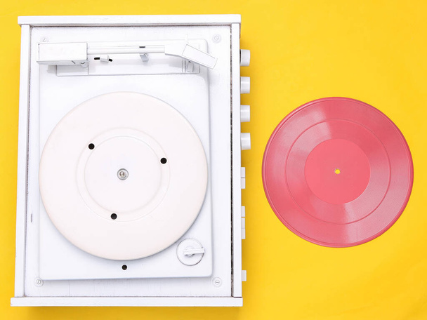 Draaitafel vinyl platenspeler op gele achtergrond. Geluidstechnologie voor DJ om muziek te mixen en af te spelen. Witte vinyl plaat met roze plaat. Minimalisme. Plat gelegd. Bovenaanzicht. - Foto, afbeelding