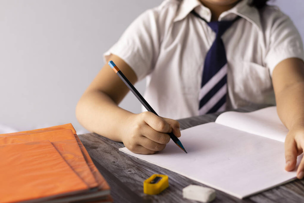 Focus selettivo a portata di mano di un bambino indiano che scrive con la matita sul taccuino indossando l'uniforme scolastica - Foto, immagini