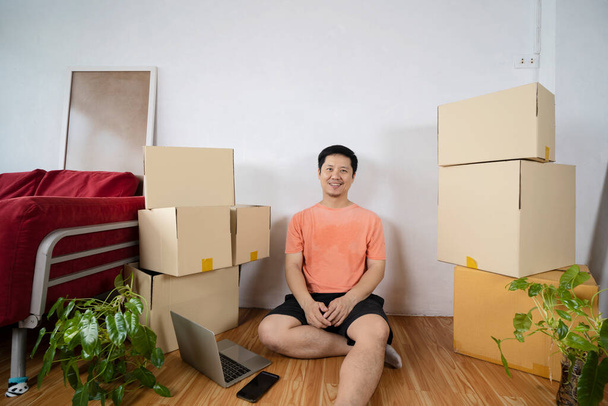 Man having break during moving to new house using laptop. Cardboard boxes - moving to a new house - Фото, изображение