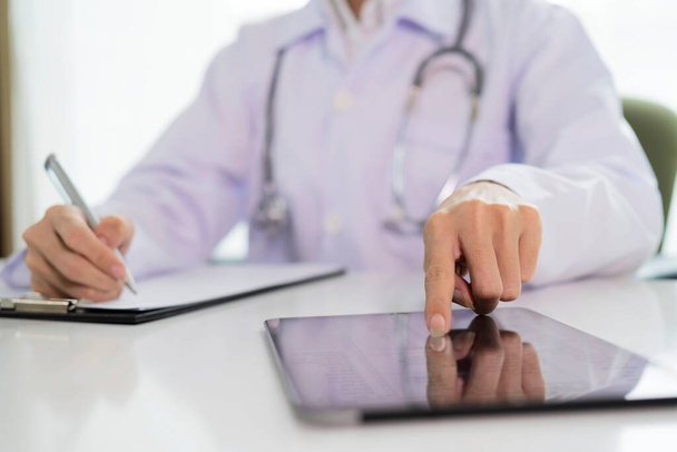 A doctor with a clipboard writing on paper and a tablet at the desk in the office Prescription medication prescribed by a doctor. - Foto, Imagem