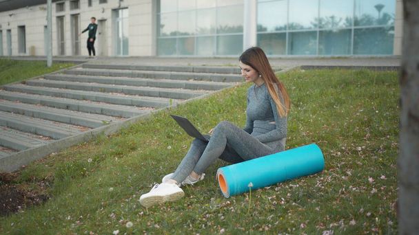 Happy woman, sitting laptop outdoor. Smiling fit girl typing on laptop computer at city background. Person working on laptop outside. Attractive girl, corporate startup office employee working outdoor - Photo, Image