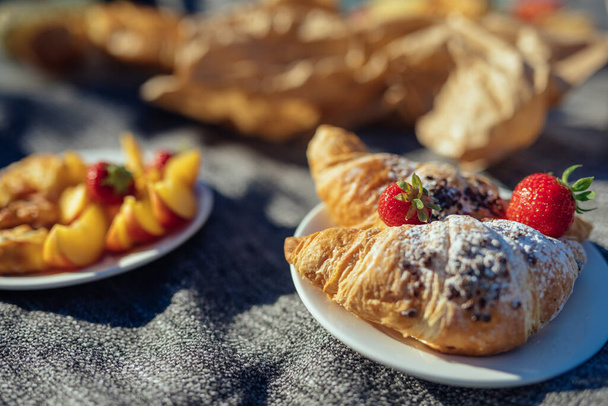 Summer picnic in nature with chocolate croissants, fresh strawberries and cut nectarine placed on white dishes - Photo, Image