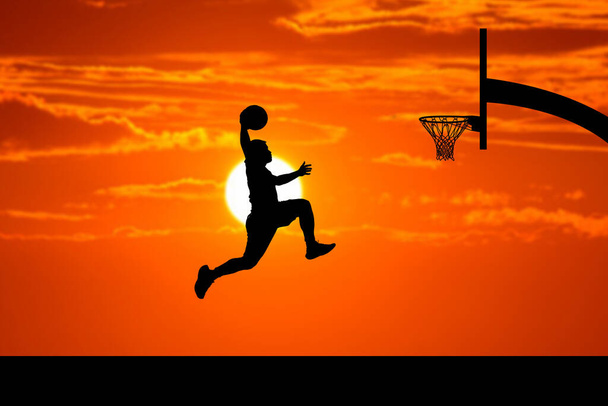 バスケットボール選手は夜に美しい屋外バスケットボールコートでダンクシルエットをジャンプします. - 写真・画像