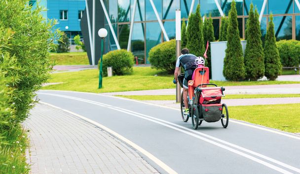 Ein Mann auf einem Fahrrad mit einem kleinen Jungen, der einen Helm im Kindersitz trägt, auf einem Radweg in der Stadt. - Foto, Bild