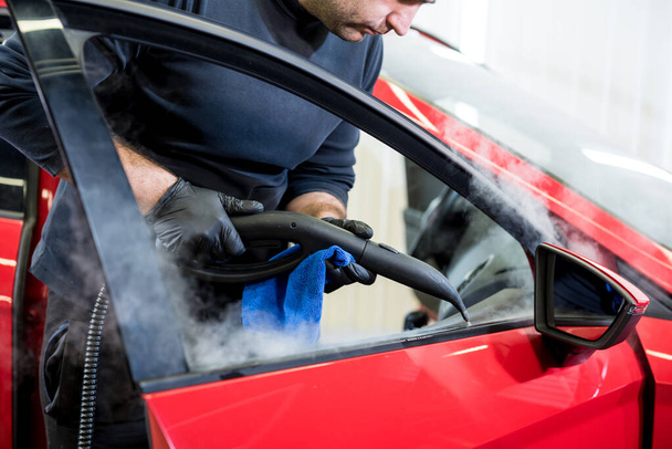 Car service worker cleans interiror with steam cleaner - Fotoğraf, Görsel