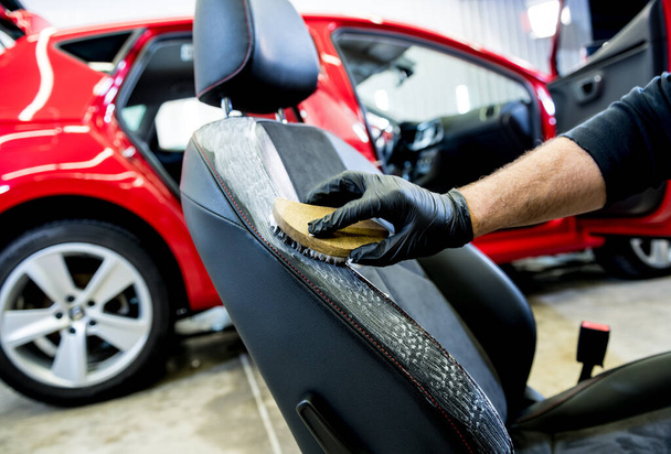 Car service worker cleans a car seat with a special brush - 写真・画像