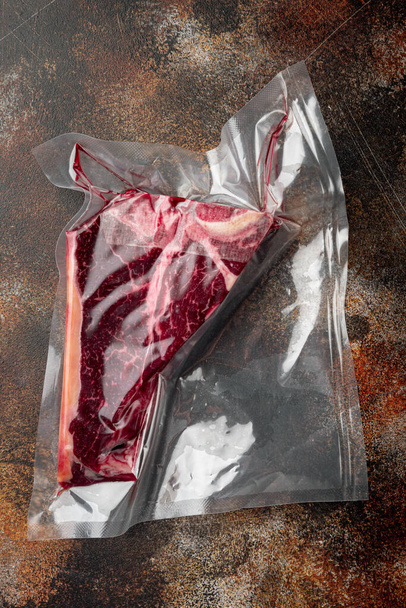 Surowy stek wołowy t-bone lub wieprzowina w próżni Zestaw opakowań, na starym ciemnym rustykalnym tle, widok z góry płaski lay - Zdjęcie, obraz