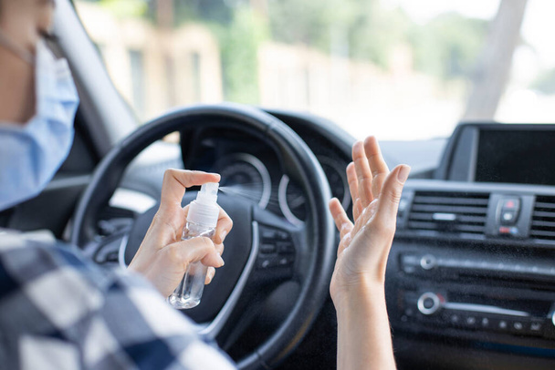 Young woman in face mask spraying hand sanitizer in the car - Foto, Imagem