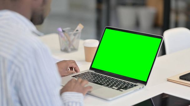 Hombre africano usando el ordenador portátil con la pantalla dominante verde del croma  - Foto, Imagen