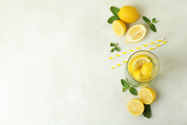 Glass of lemonade, straws and lemons on white textured table - Фото, изображение